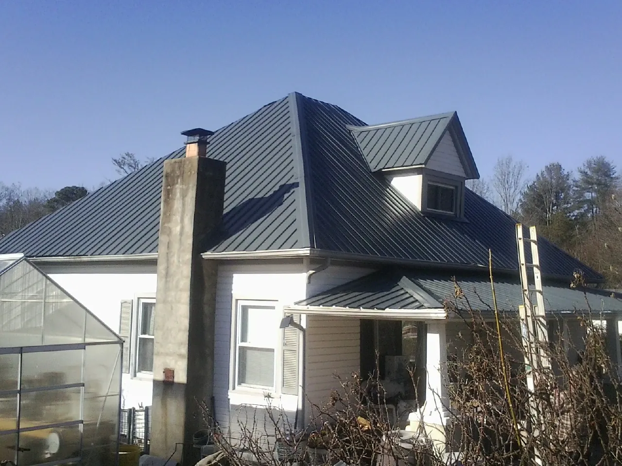 Dark blue standing seam metal roof on a white farmhouse with dormer — Slate & Tile Roof Repair by Roofing Brothers in Crestline